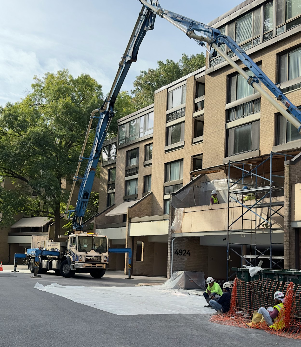Concrete pump truck boom extends to apartment building renovation site.